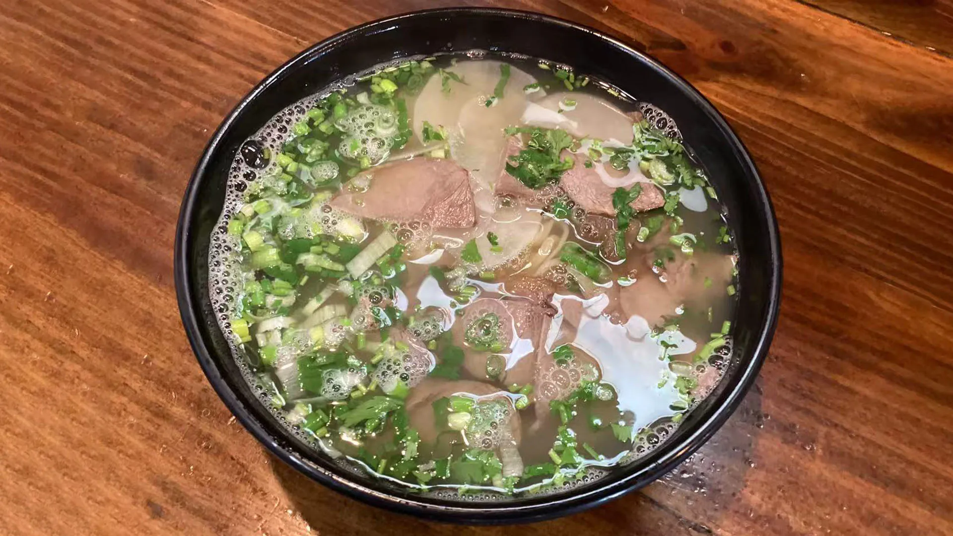 Classic clear Lan Zhou beef noodle soup topped with beef and green onions at Noodle Man，a Chinese Restaurant in Virginia Beach