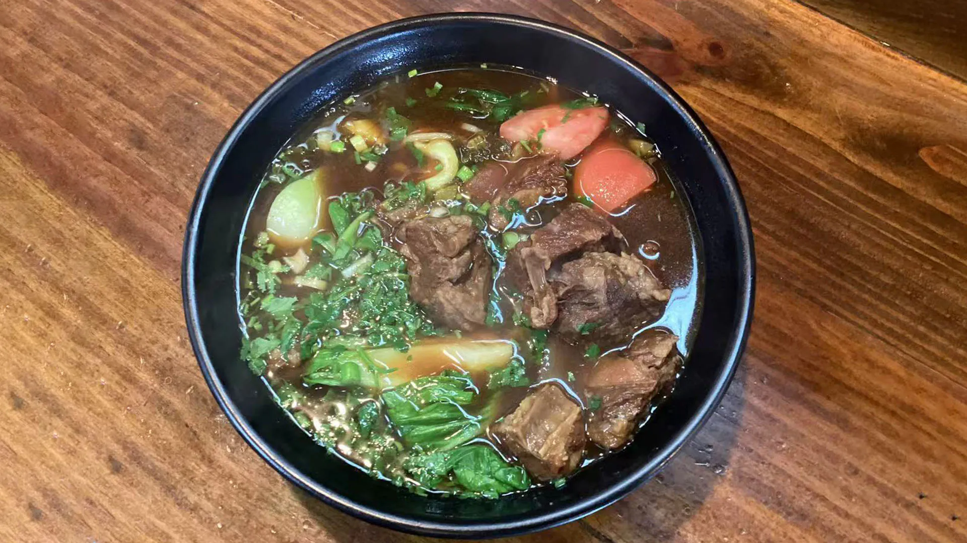 Sweet tomato beef brisket noodle soup with fresh leafy greens at Noodle Man，a Chinese Restaurant in Virginia Beach