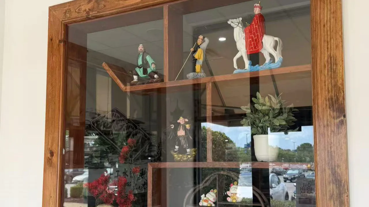 Wooden display cabinet with Journey to the West figurines and lucky cat ornaments at Noodle Man，a Chinese Restaurant in Virginia Beach